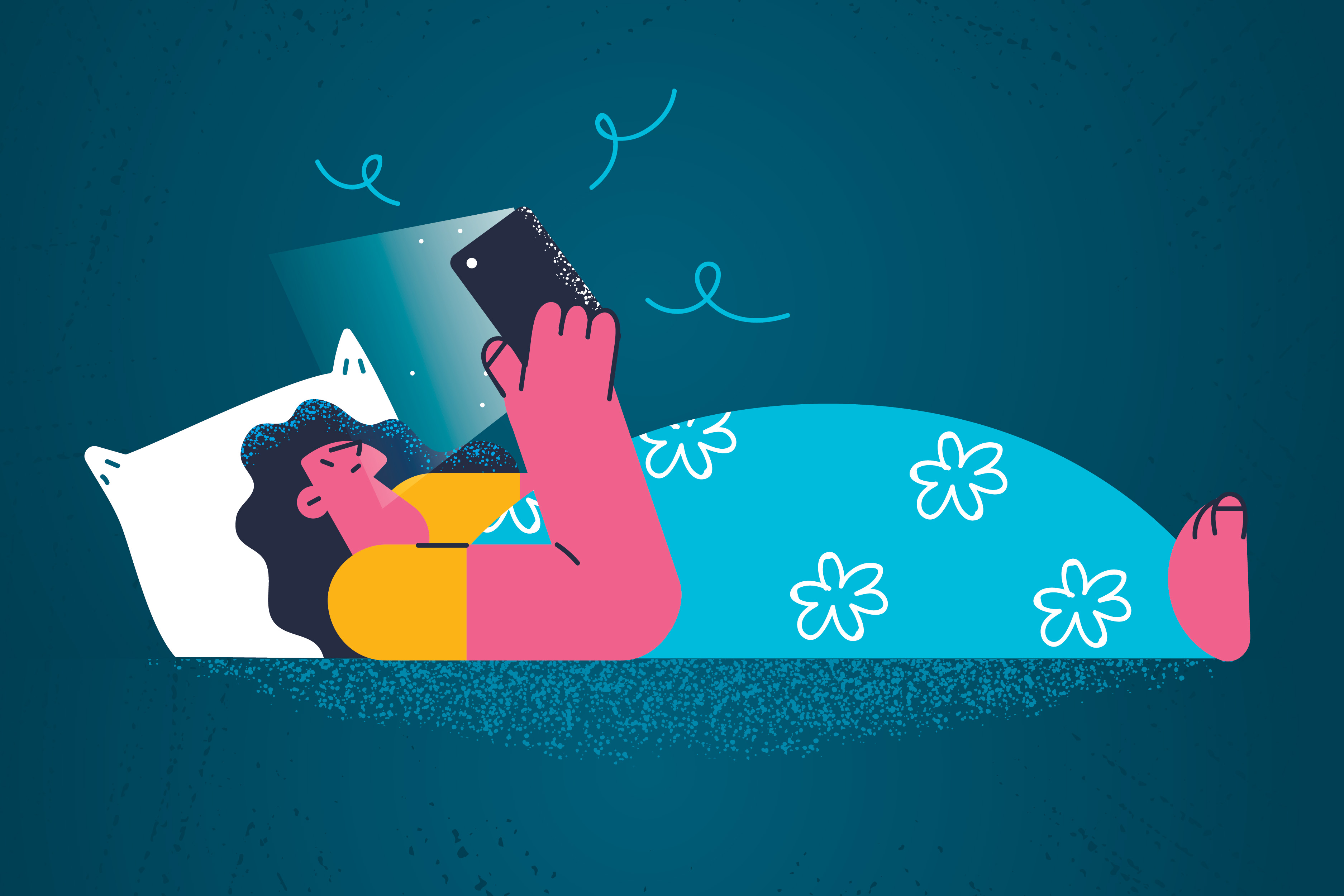 A woman lies in bed looking at a smartphone while tucked under a blue blanket with flowers on it.